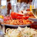 Lobster pasta and a glass of wine in the foreground with several other dishes on the table.