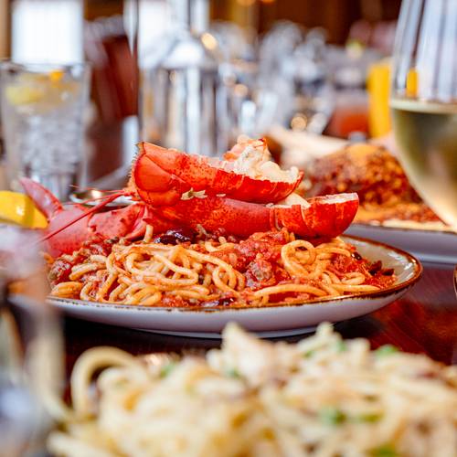 Lobster pasta and a glass of wine in the foreground with several other dishes on the table.
