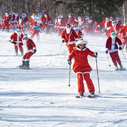 A group of skiiers skiing down a trail wearing Santa suits at Sunday River.
