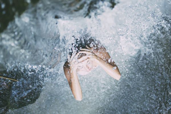 A woman sitting under a waterfall with water coming down.