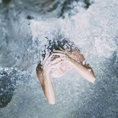 A woman sitting under a waterfall with water coming down.