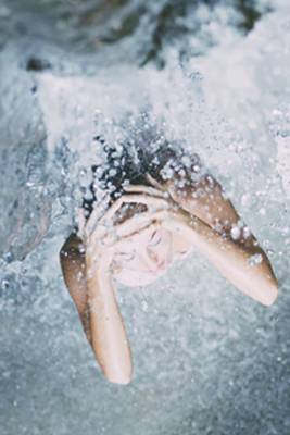 A woman sitting under a waterfall with water coming down.