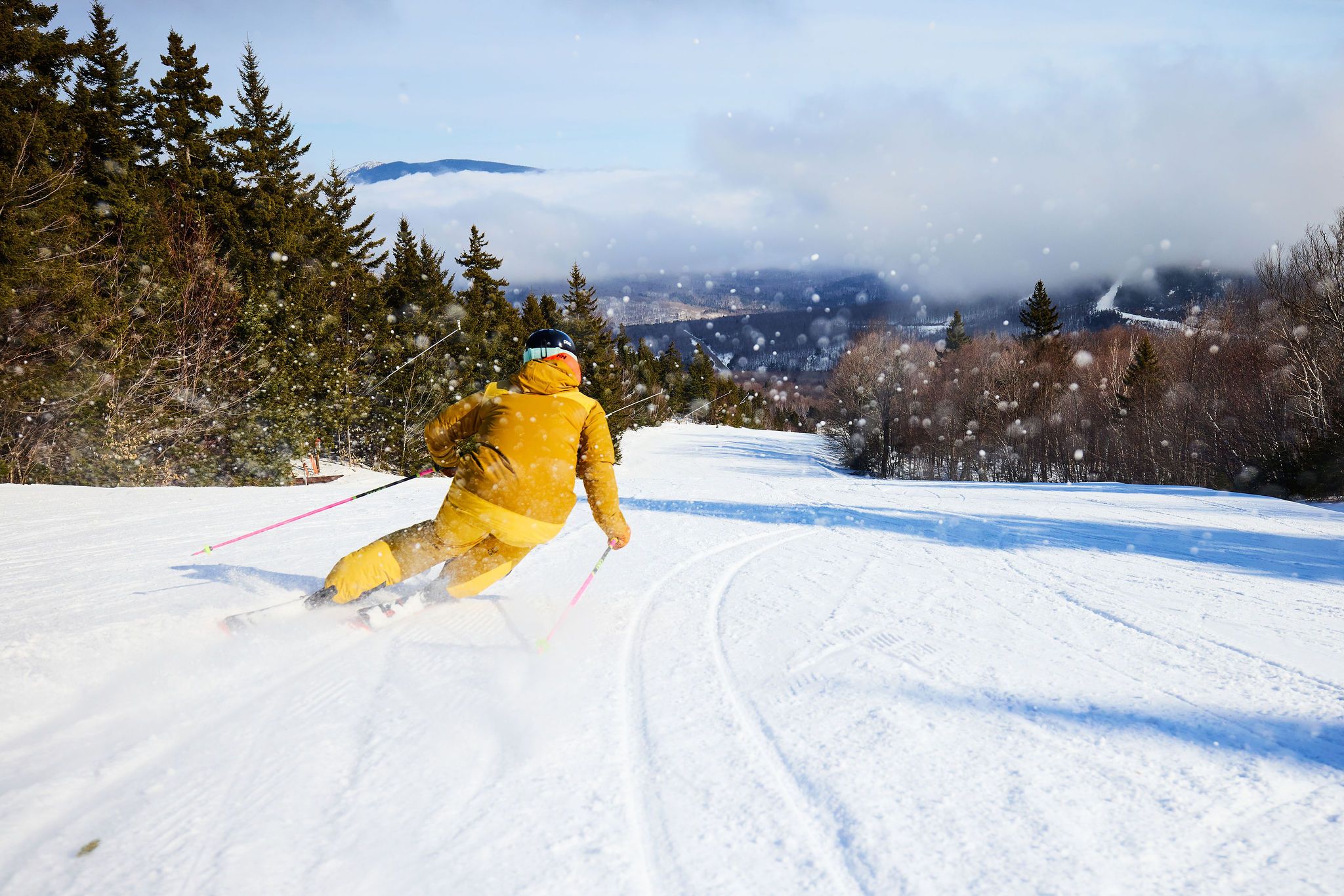 A woman in a yellow ski jacket skiing down a trail at Sunday River.