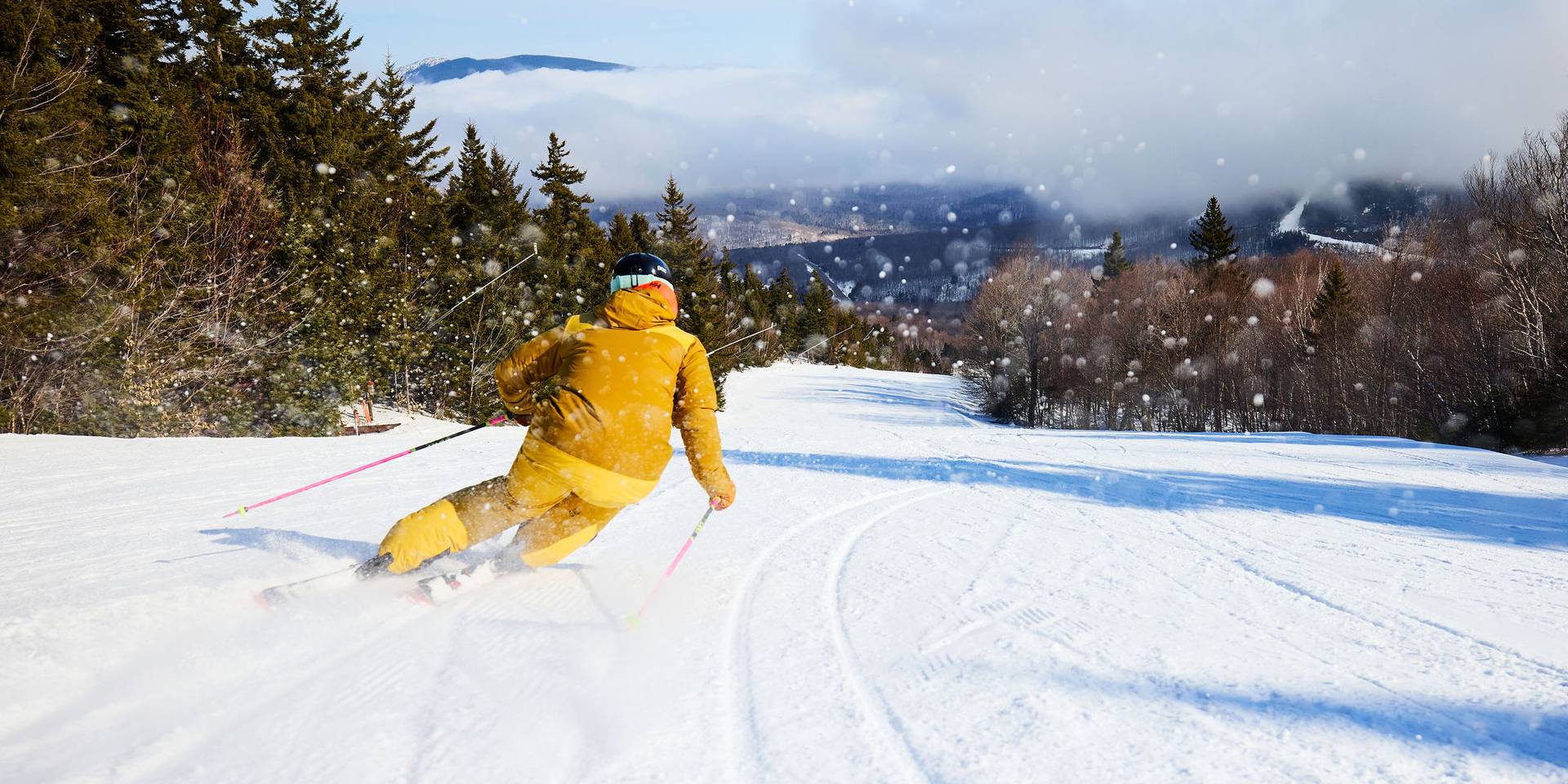A woman in a yellow ski jacket skiing down a trail at Sunday River.