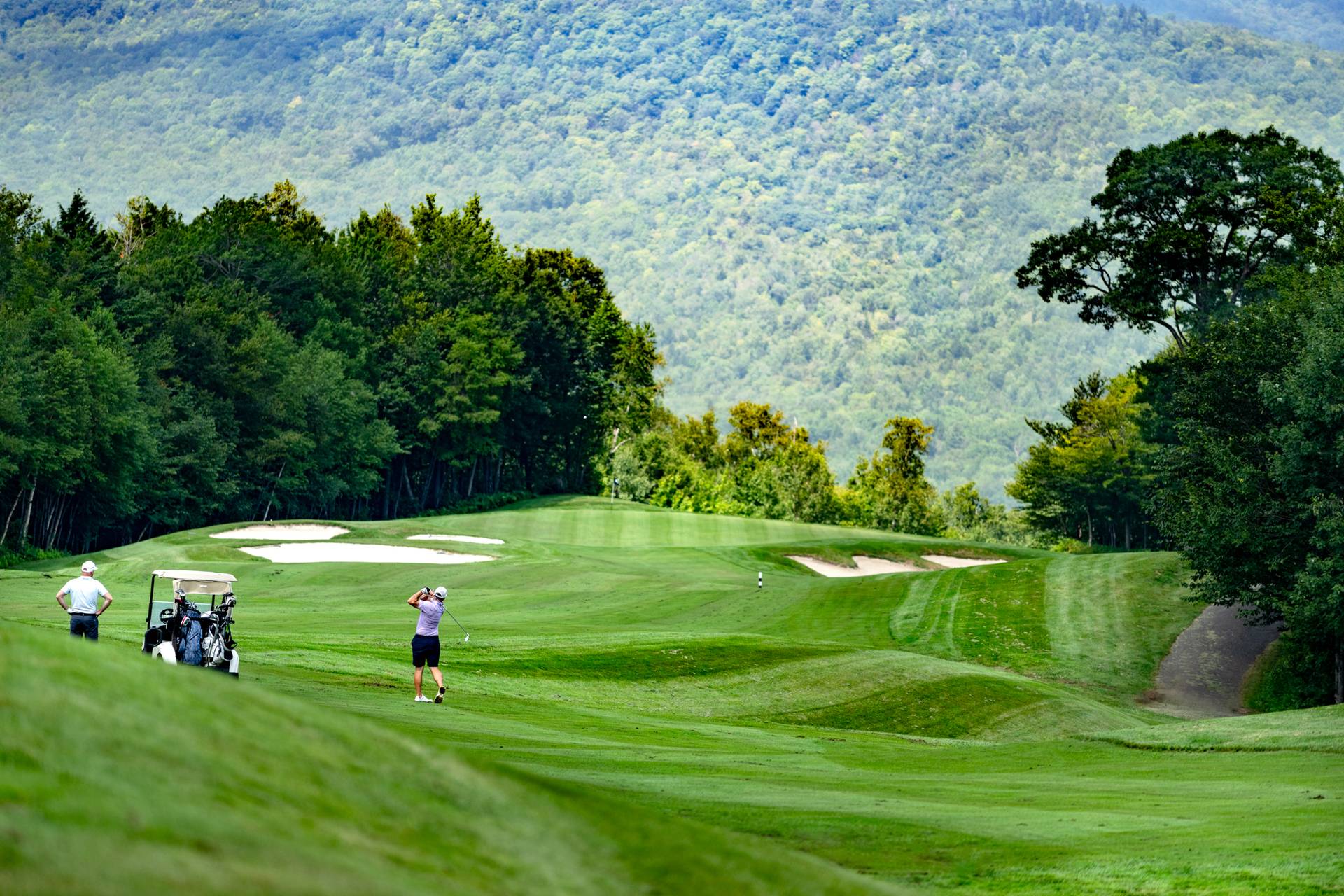 Some golfers playing a round at the Sunday River Golf Club, with mountain views, in the summer.