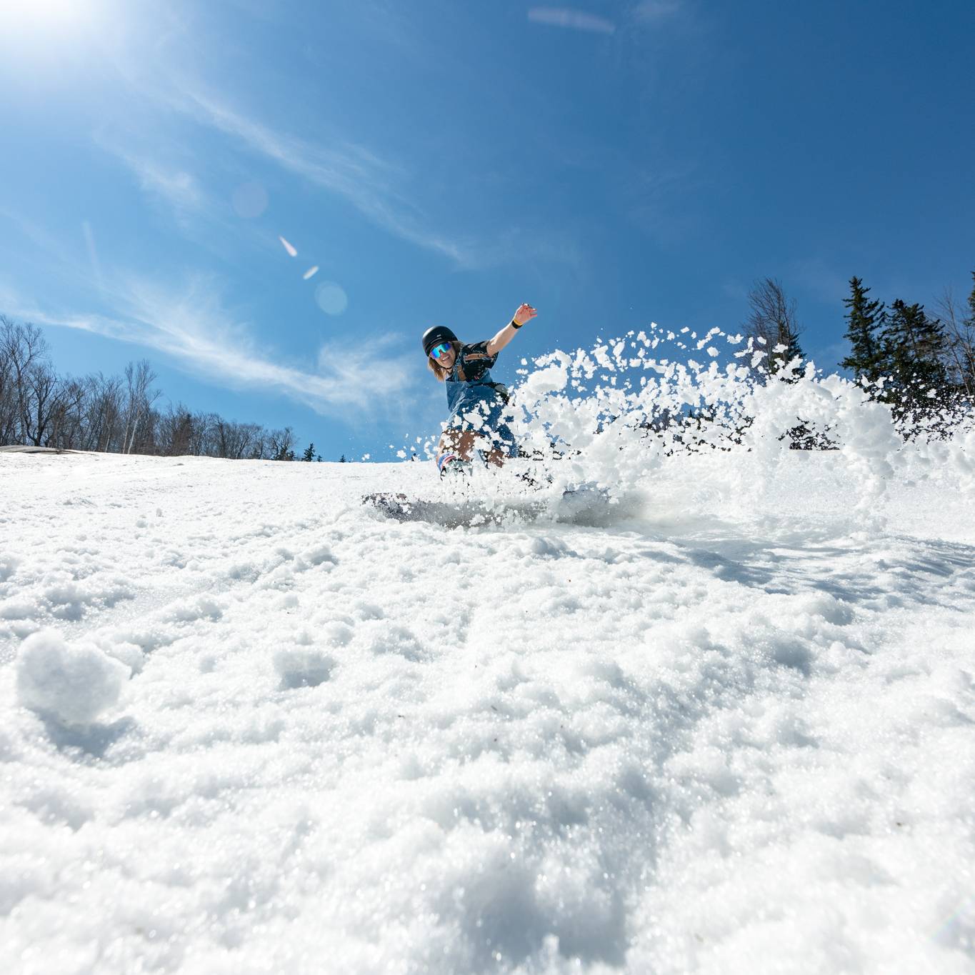 A snowboarder riding in some soft spring snow, with the sun shining, at Sunday River.