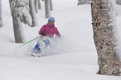 A skier skiing in powder in the woods of Sunday River.