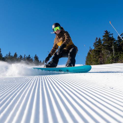 A snowboarder smiling will turning on a trail in the winter at Sunday River.