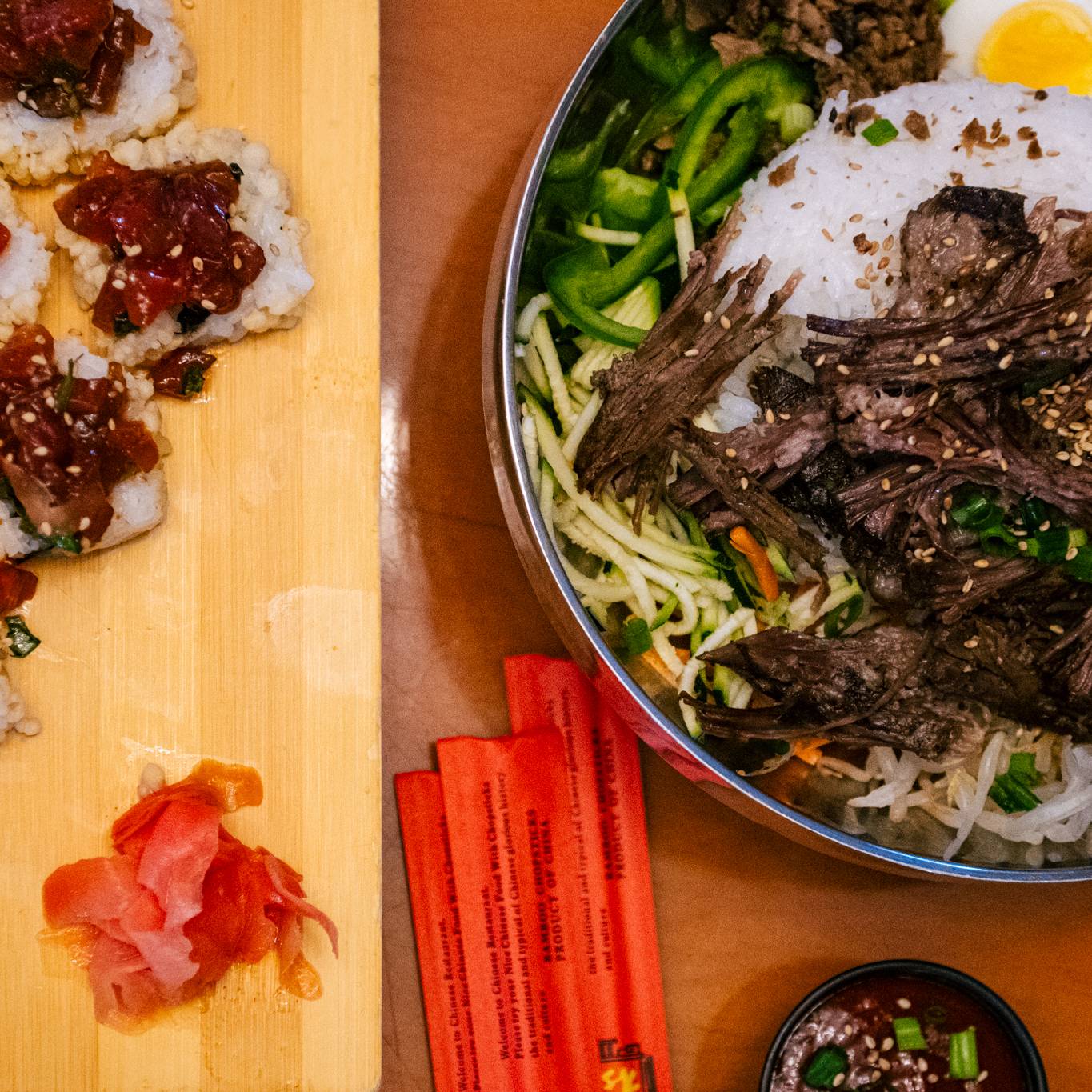 A bowl of beef, rice, and vegetables and a plate with sushi rolls.