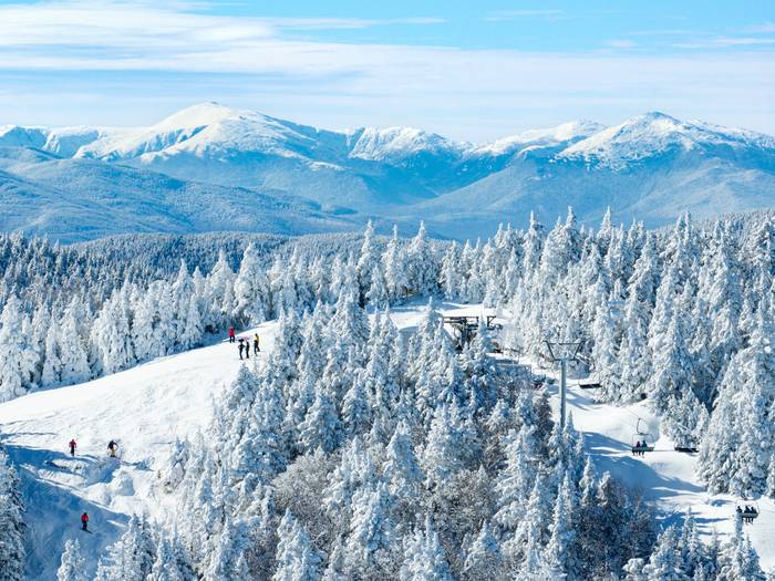 Snow trees and trails at the top of Oz peak at Sunday River, with mountains in the background.