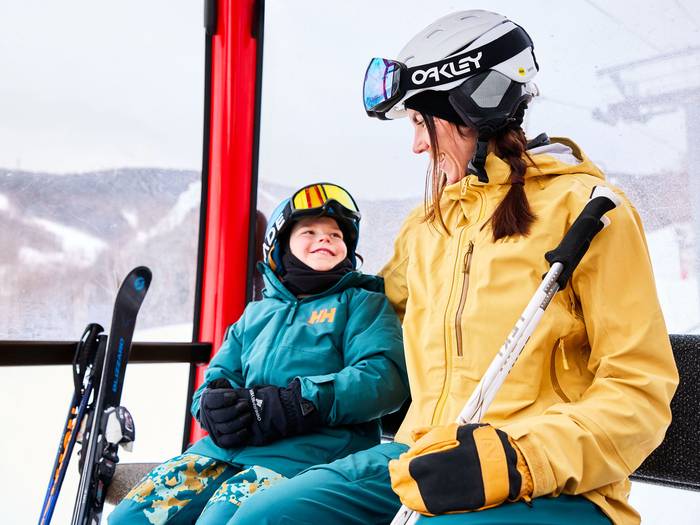 A mom and son sitting in the Chondola at Sunday River smiling at each other.