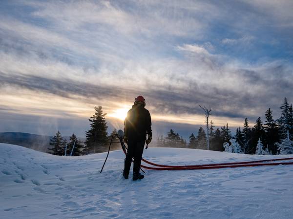 A snowmaker at Sunday River, looking at a snowgun as the sun rises.