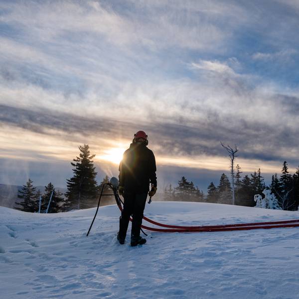 A snowmaker at Sunday River, looking at a snowgun as the sun rises.