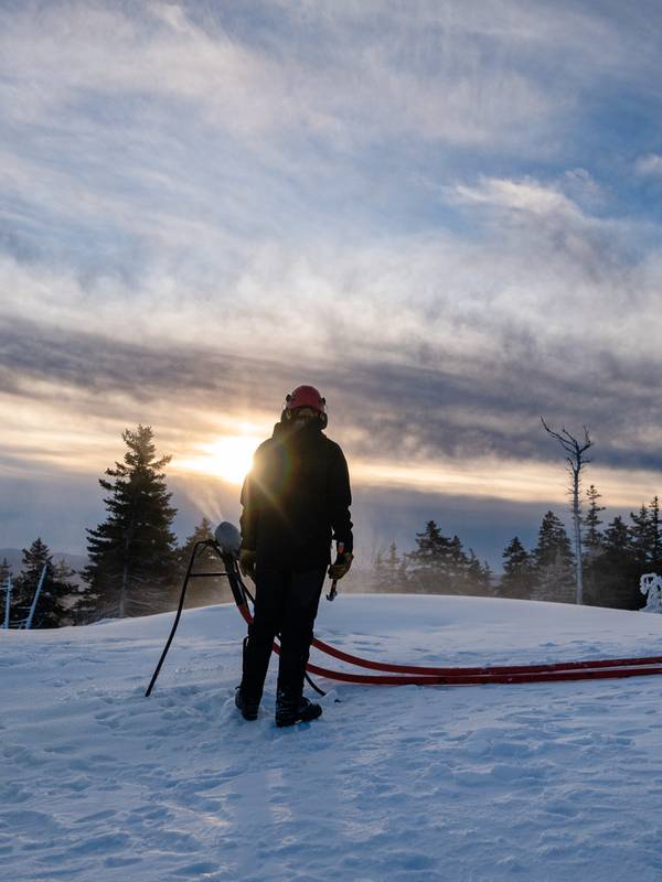 A snowmaker at Sunday River, looking at a snowgun as the sun rises.