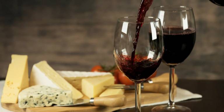 Wine being poured into a glass with cheese in the background.