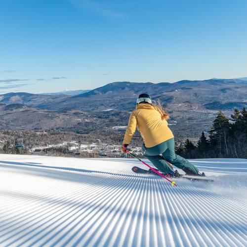 A woman skiing in a yellow jacket and blue pants down a trail at Sunday River.