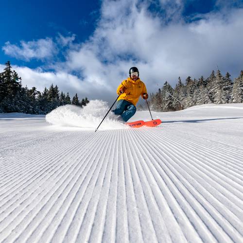 A man skiing down a trail at Sunday River on fresh corduroy.