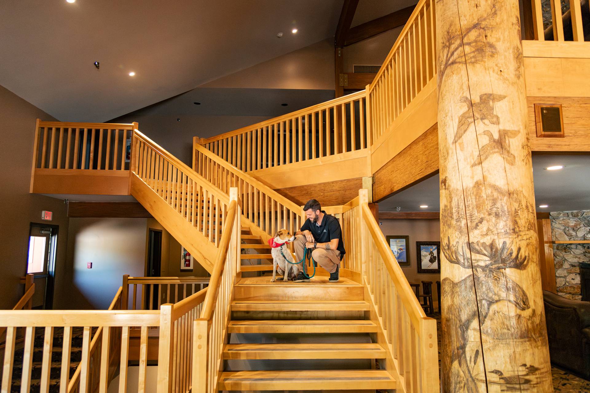 A man and a dog sitting on the grand stairway inside the Snow Cap Inn at Sunday River.