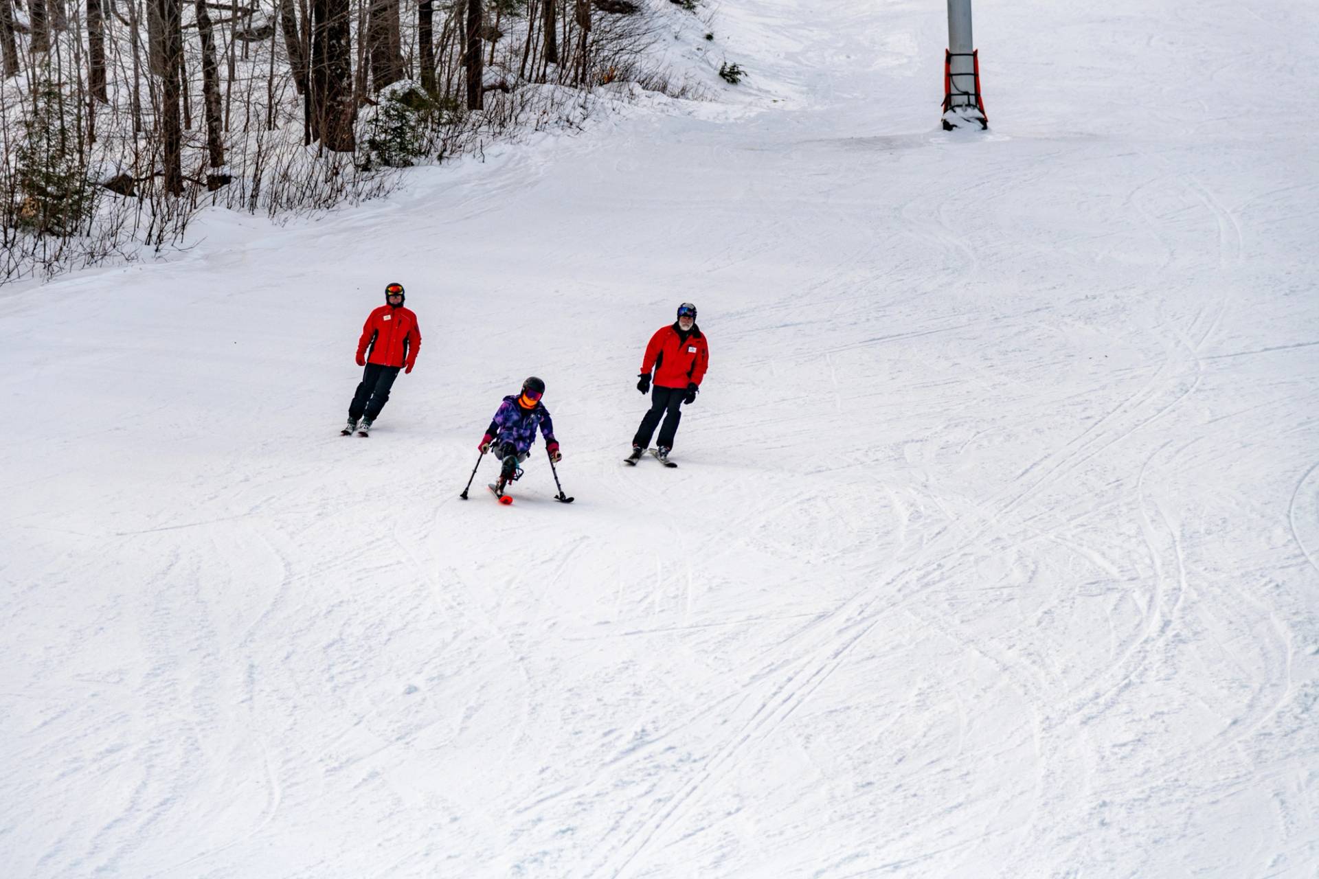 A skier and Maine Adaptive coaches skiing down a trail.