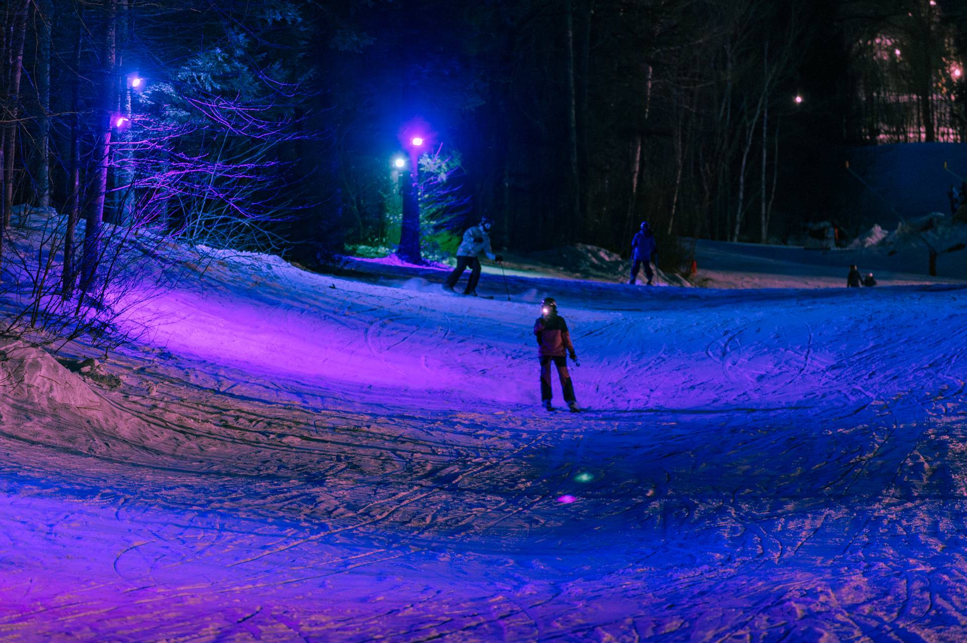 A kid skiing under colorful lights at Sunday River during twilight skiing.