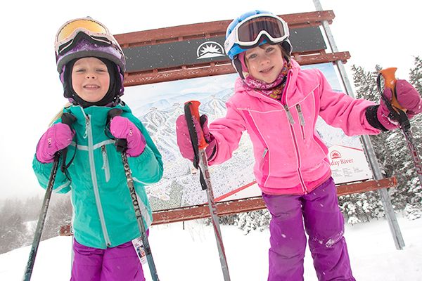 Two kids in ski gear in front of a trail sign at Sunday River.