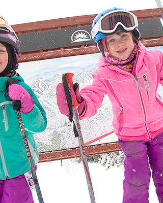 Two kids in ski gear in front of a trail sign at Sunday River.