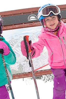 Two little girls posing in front of a sign, on skis, at Sunday River Resort.