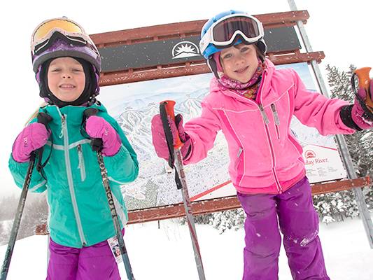 Two kids in ski gear in front of a trail sign at Sunday River.