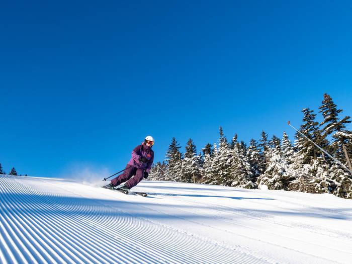 Skier on corduroy with a blue sky behind.
