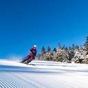 A woman skiing down a trail at Sunday River with blue skies and wearing a purple kit.