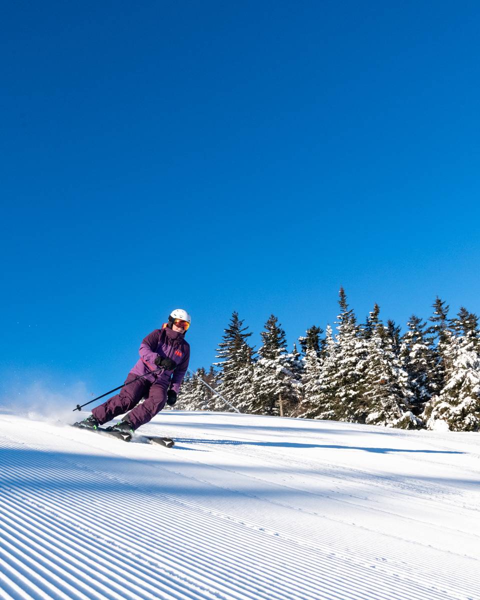 Skier on corduroy with a blue sky behind.
