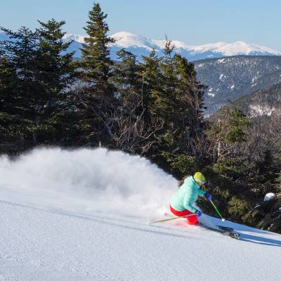 A skier cruising on a trail, with snow trailing behind her, at Sunday River.