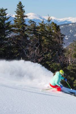 A skier cruising on a trail, with snow trailing behind her, at Sunday River.