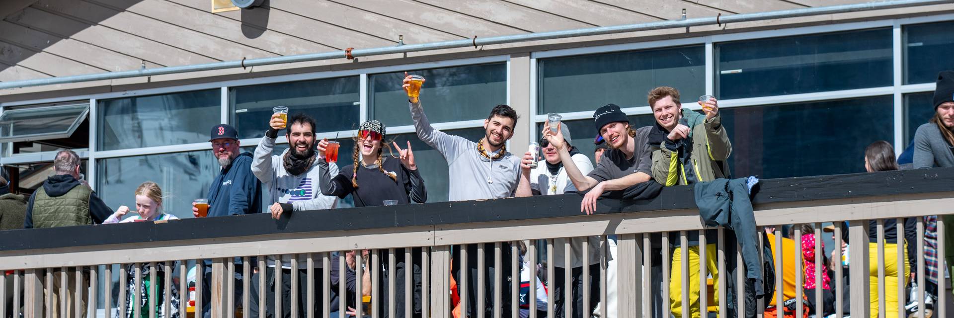 People posing for a photo with their drinks on the Foggy Goggle deck at Sunday River.
