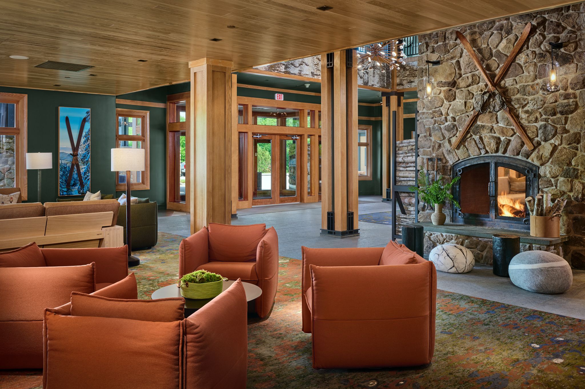The lobby of The Jordan at Sunday River, with a fire roaring, orange chairs, surrounded by a cozy Maine woods vibe.