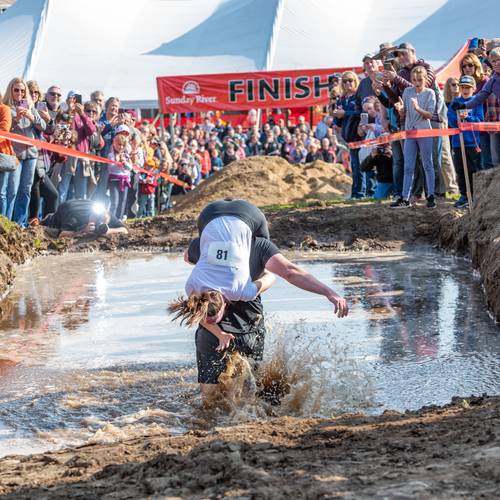 A woman on a man's back, splashing through mud, while competing in the North American Wife Carrying Championship at Sunday River.