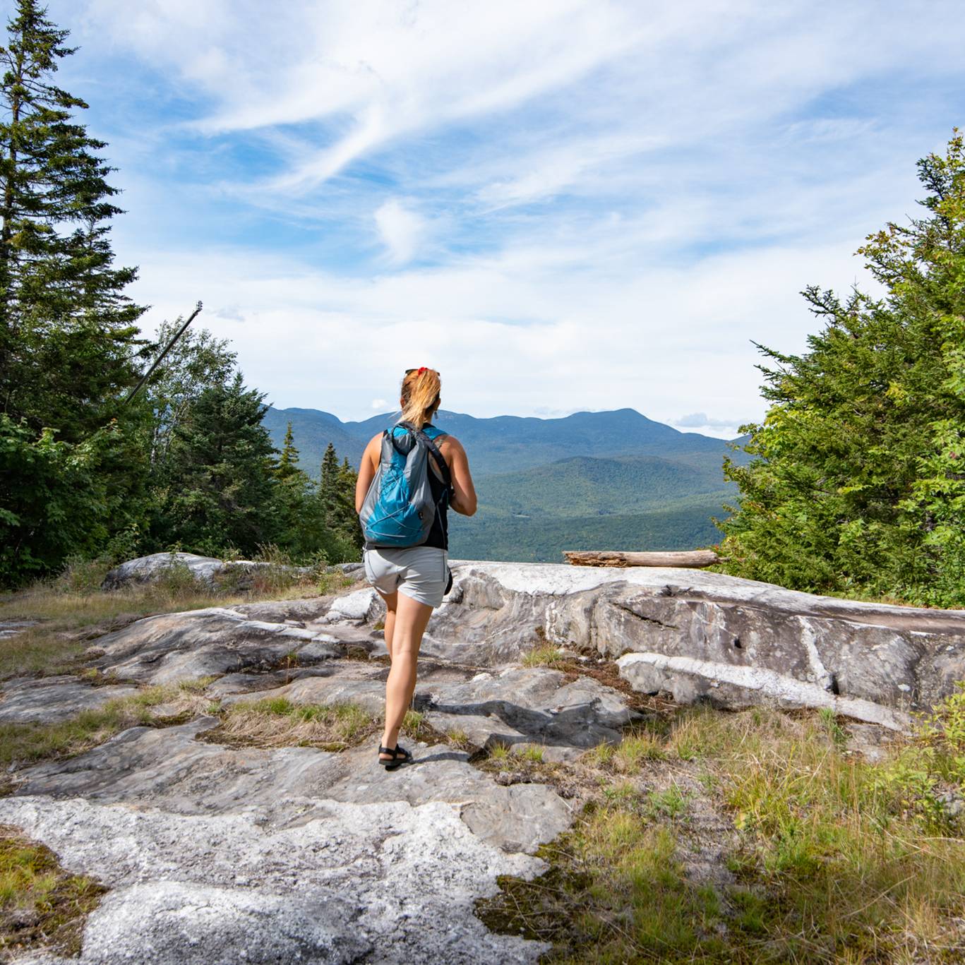 A woman hiking in with a blue backpack on a sunny day.