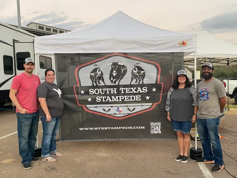 Four adults stand beside a South Texas Stampede banner under a white canopy.
