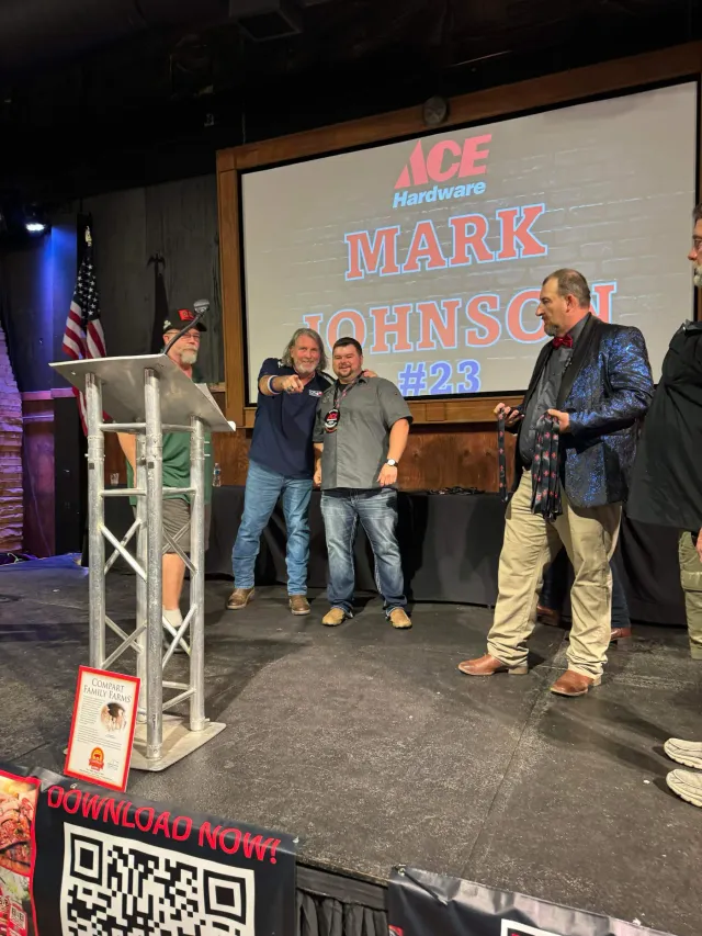 A presenter stands beside two participants on an awards stage.