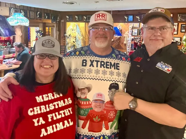 Three adults wearing festive clothing pose together indoors.