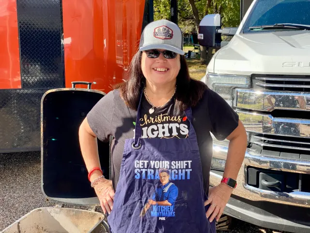 A woman wearing a Christmas lights shirt stands beside a truck.