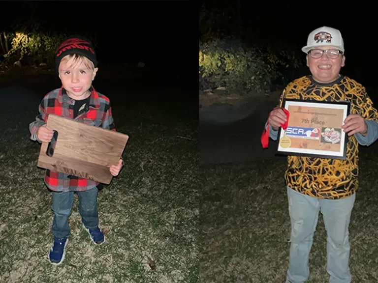 Two children hold awards while standing outdoors at night.