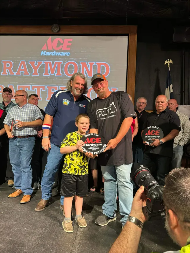 Two men and a child pose with an award in front of a projection screen.