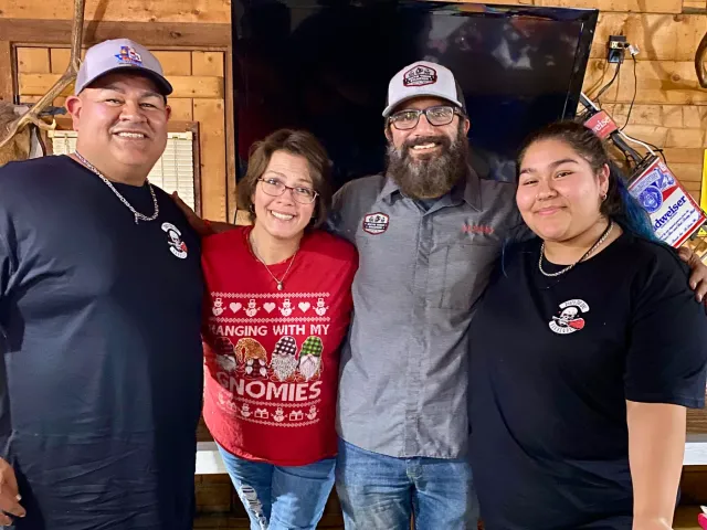 Four adults stand together for a group photo indoors.