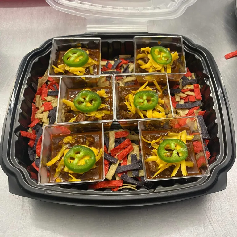 Six small servings topped with sliced jalapeños are arranged in a black tray.