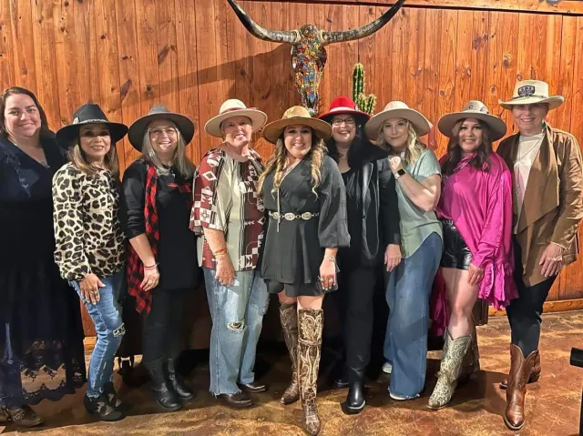 A group poses beneath mounted longhorn horns against a wood-paneled wall.