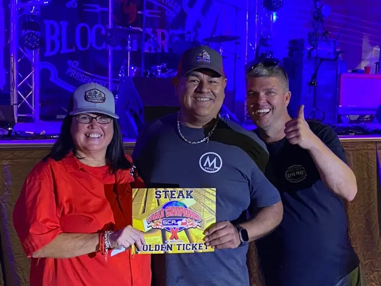 Three adults pose with a Steak Golden Ticket beneath blue stage lights.