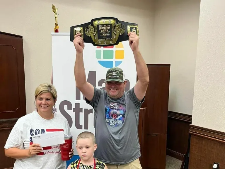 A man raises a championship belt above his head beside a woman and a child.