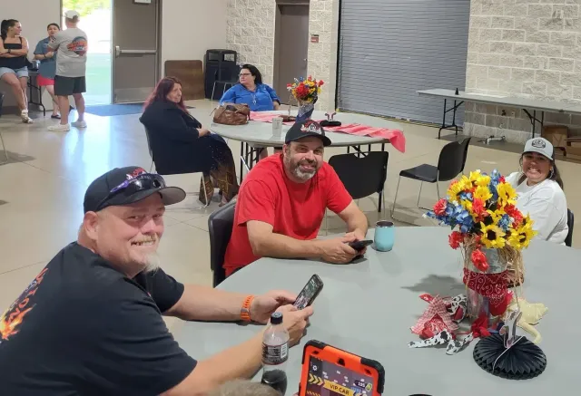 Two men smile from a round table while other guests sit behind them.