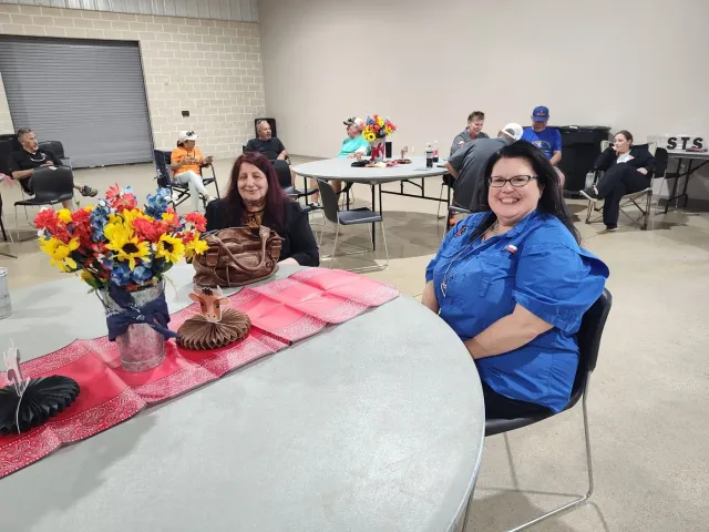 Two women sit at a round table decorated with flowers and a pink runner.